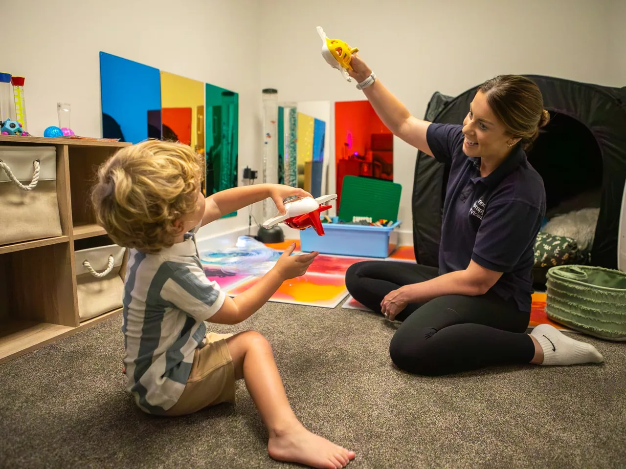 A Connect therapist and a young boy playing together with toy aeroplanes in the sensory room