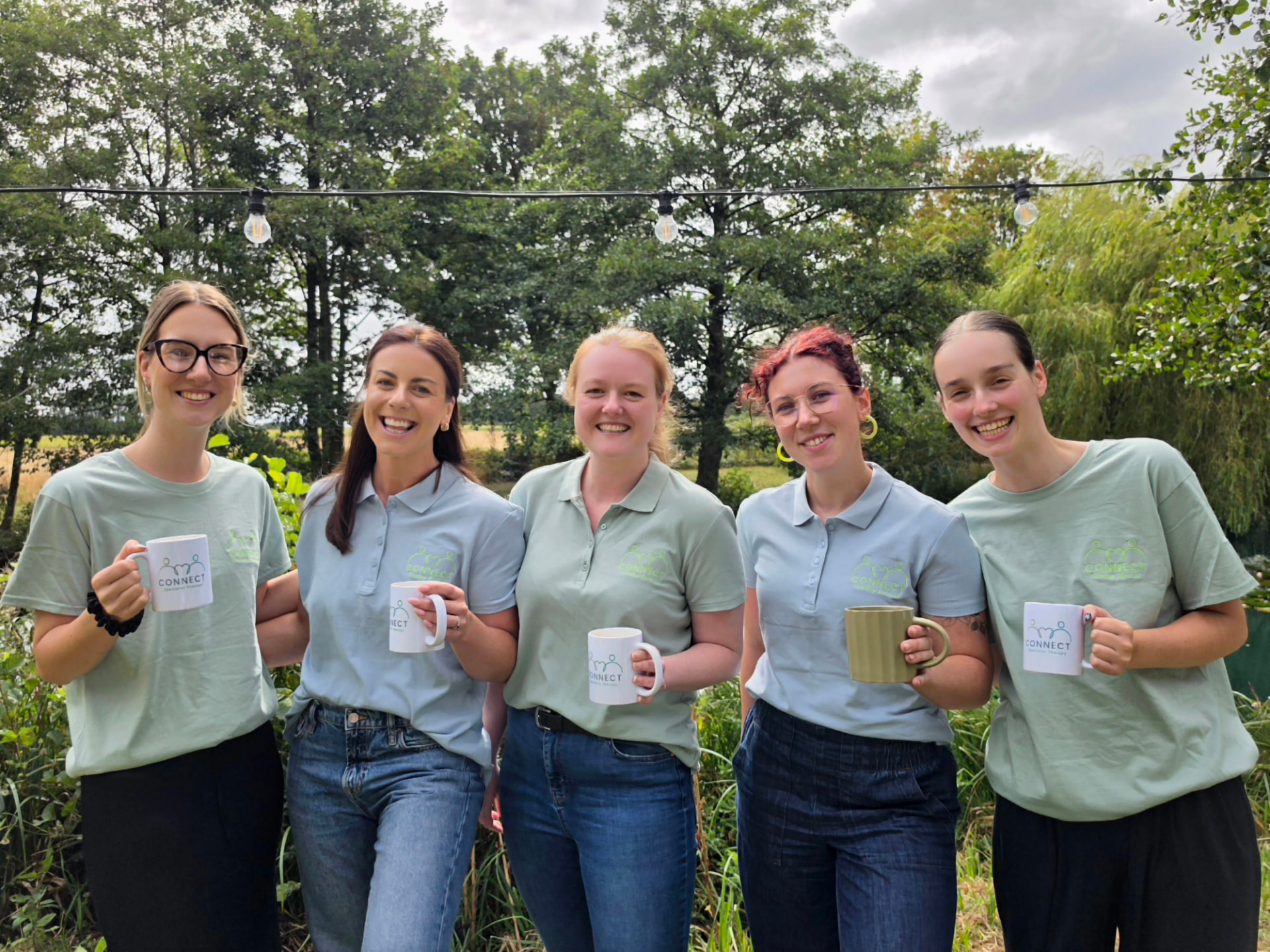 The Connect team standing together outdoors in branded shirts, smiling and holding Connect mugs