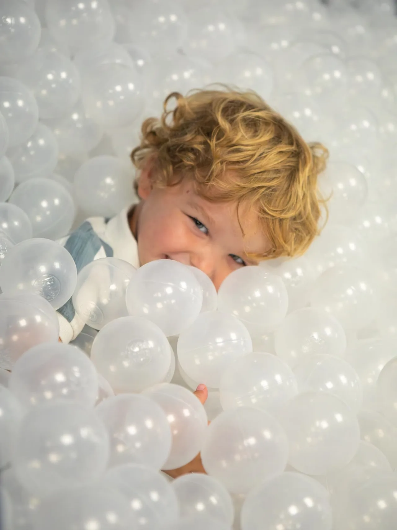 A smiling toddler peeking out from the ball pit in the Connect soft play room