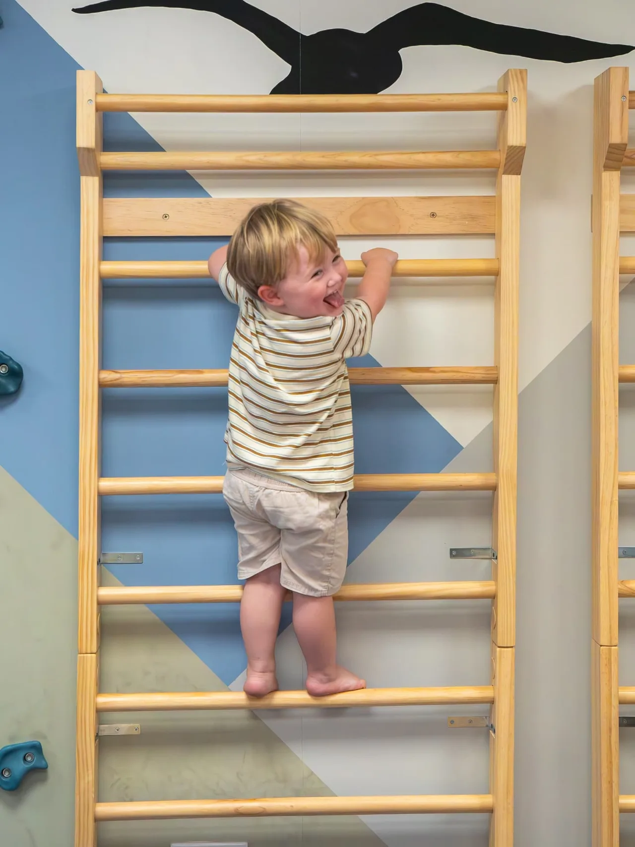A laughing toddler climbing the wooden ladder frame