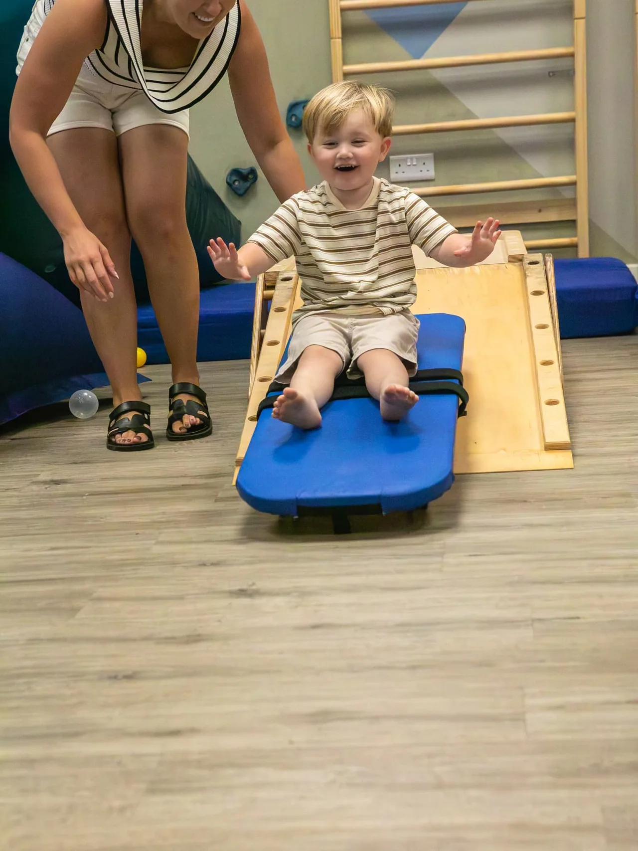 A laughing toddler on a scooter board with the therapist