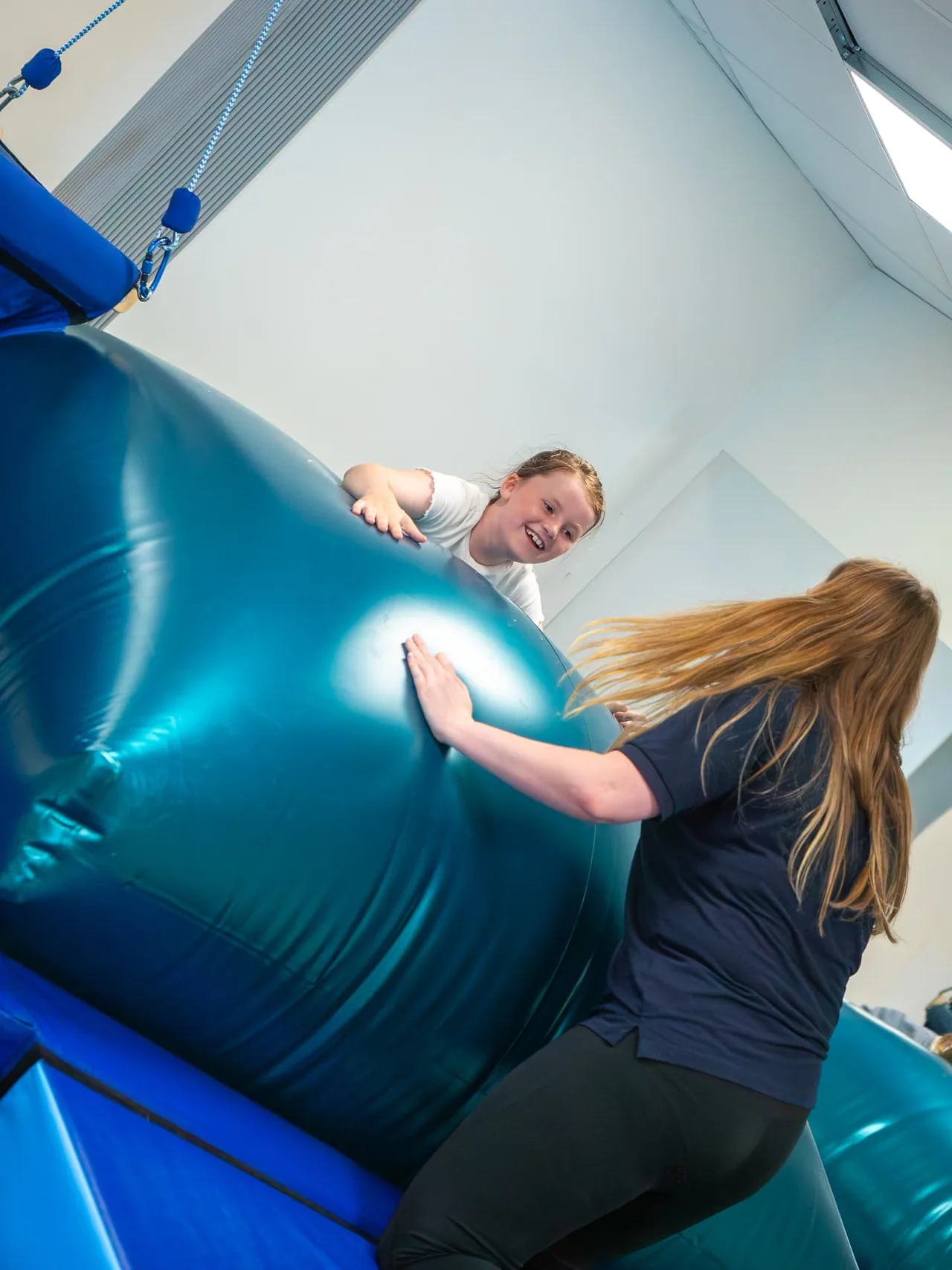 A girl lying over a therapy ball with the therapist in the soft play room