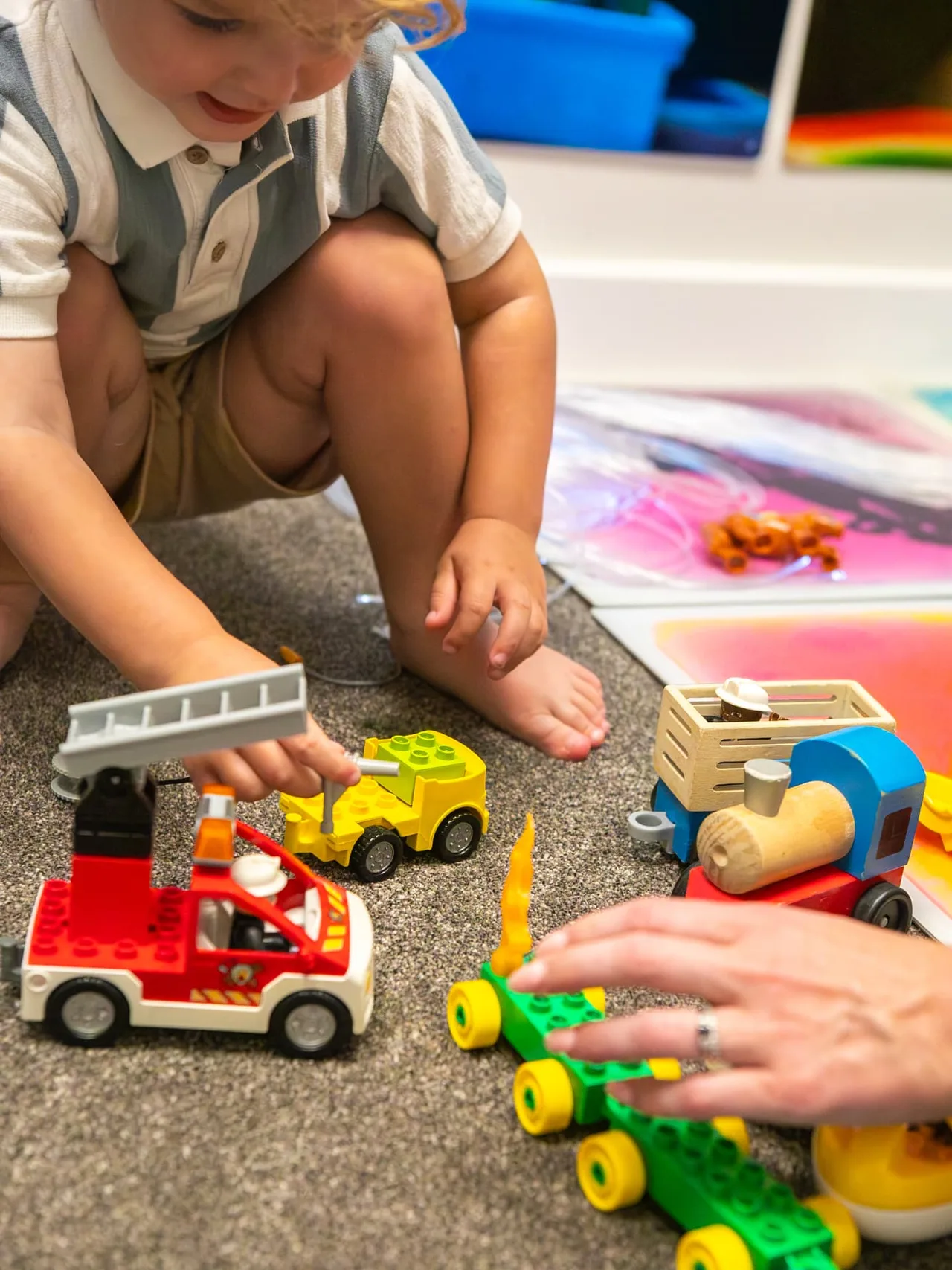 A child and therapist playing with toy vehicles on the carpet