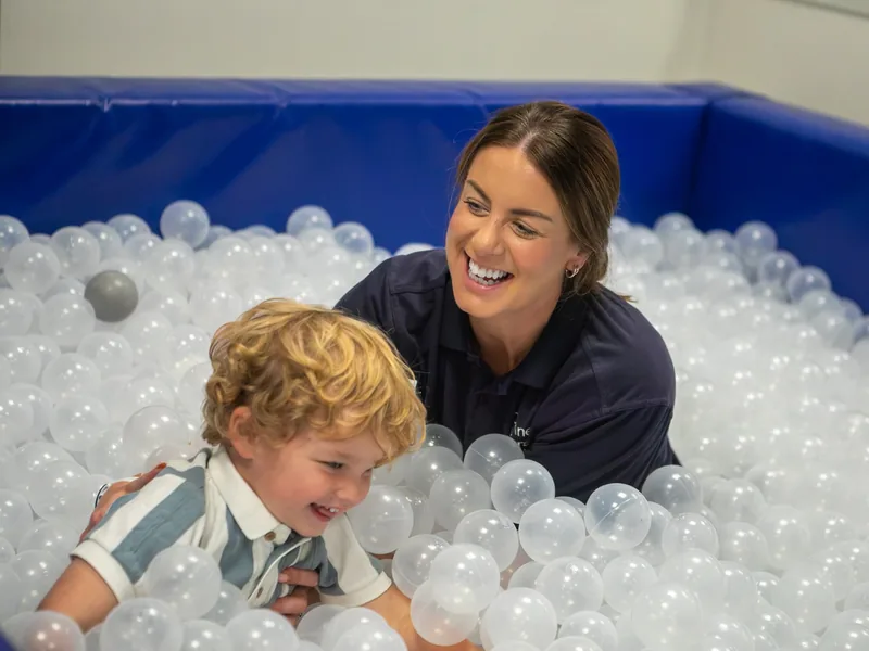 A Connect therapist and a laughing toddler playing together in the ball pit