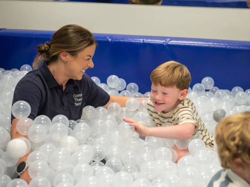 A Connect therapist and a smiling young boy playing together in the ball pit