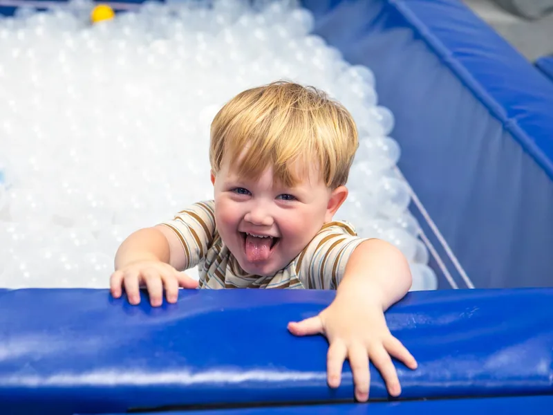 A laughing toddler peering over the edge of the ball pit at the Connect clinic