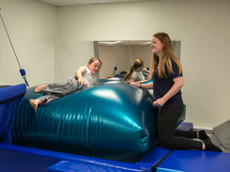 A smiling girl lying over a large therapy ball with a Connect therapist kneeling beside her
