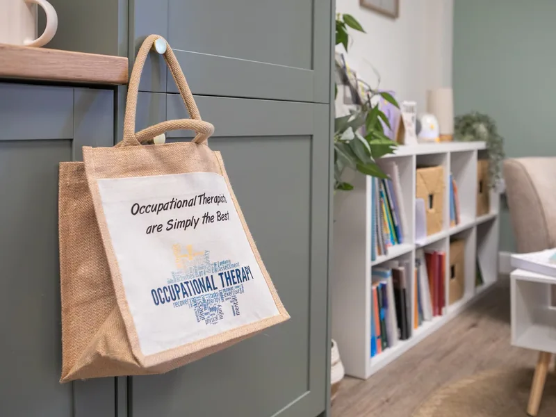 A Connect tote bag reading 'Occupational Therapists are Simply the Best' hanging on a cabinet in the clinic